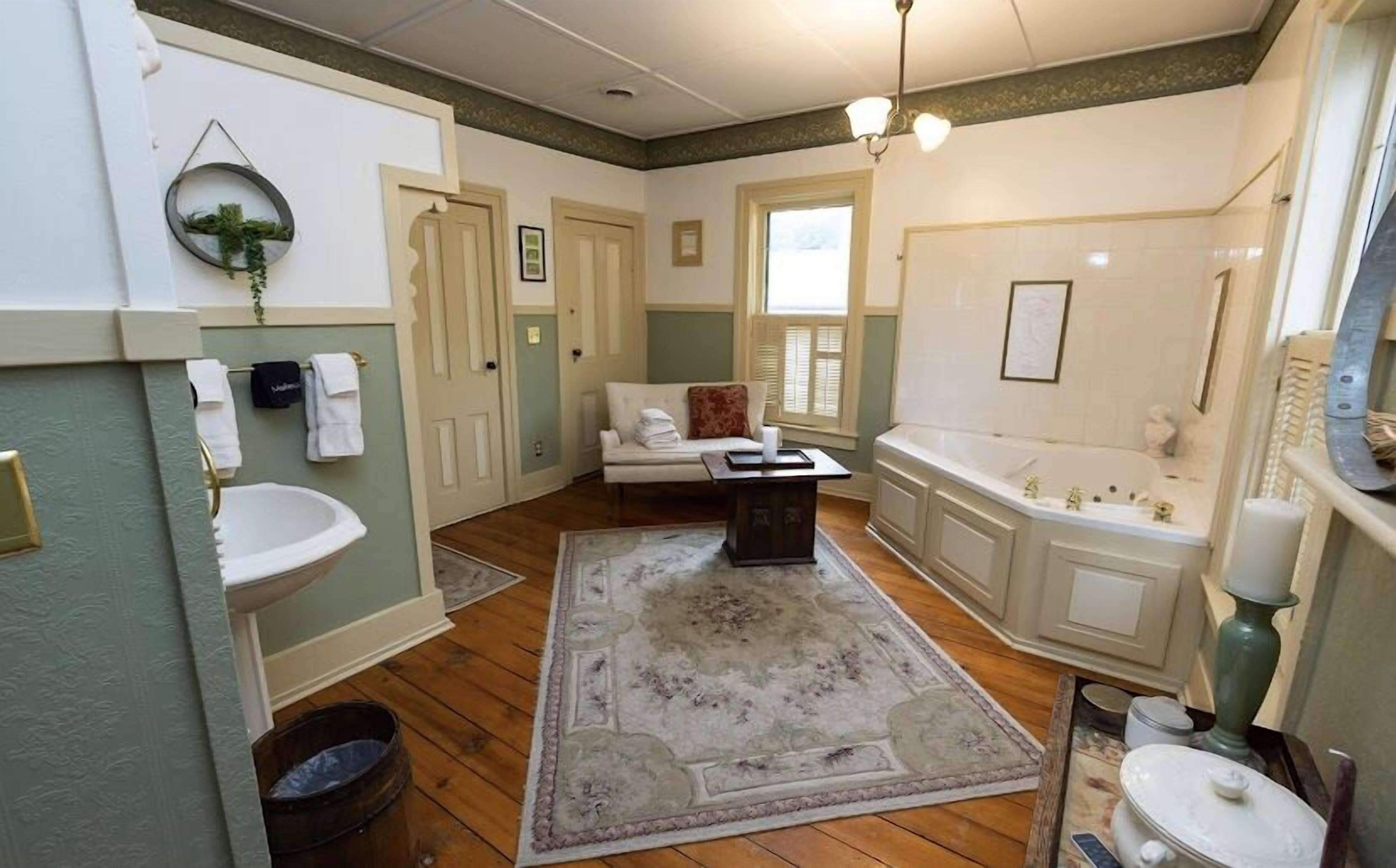 A spacious bathroom with a large bathtub, a sink, and a toilet. There is a wooden floor and a rug.