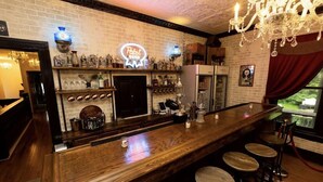 Zona de bar con mostrador de madera, taburetes, estantes con botellas y un letrero de neón.
