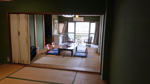 A traditional Japanese room with tatami flooring, a low table with cushions, and a sliding door leading to a balcony with a view.