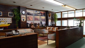 A reception area with a brick wall, wooden reception desk, several seating areas with cushioned chairs, a clock, framed pictures, and potted plants.