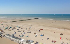 Una playa con un muelle largo que se adentra en el agua, numerosas sombrillas y gente relajándose sobre la arena.