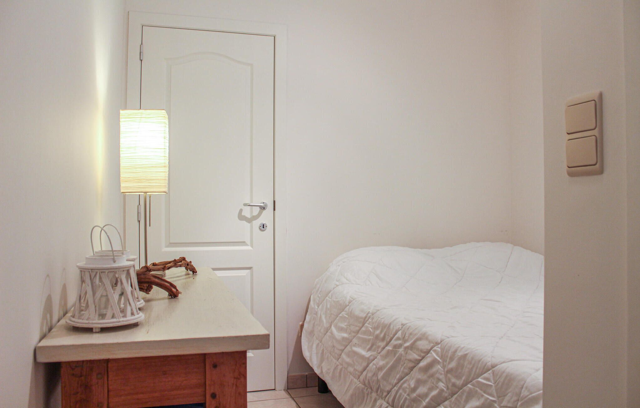 Un dormitori amb un llit, una tauleta de nit amb una làmpada i una porta.