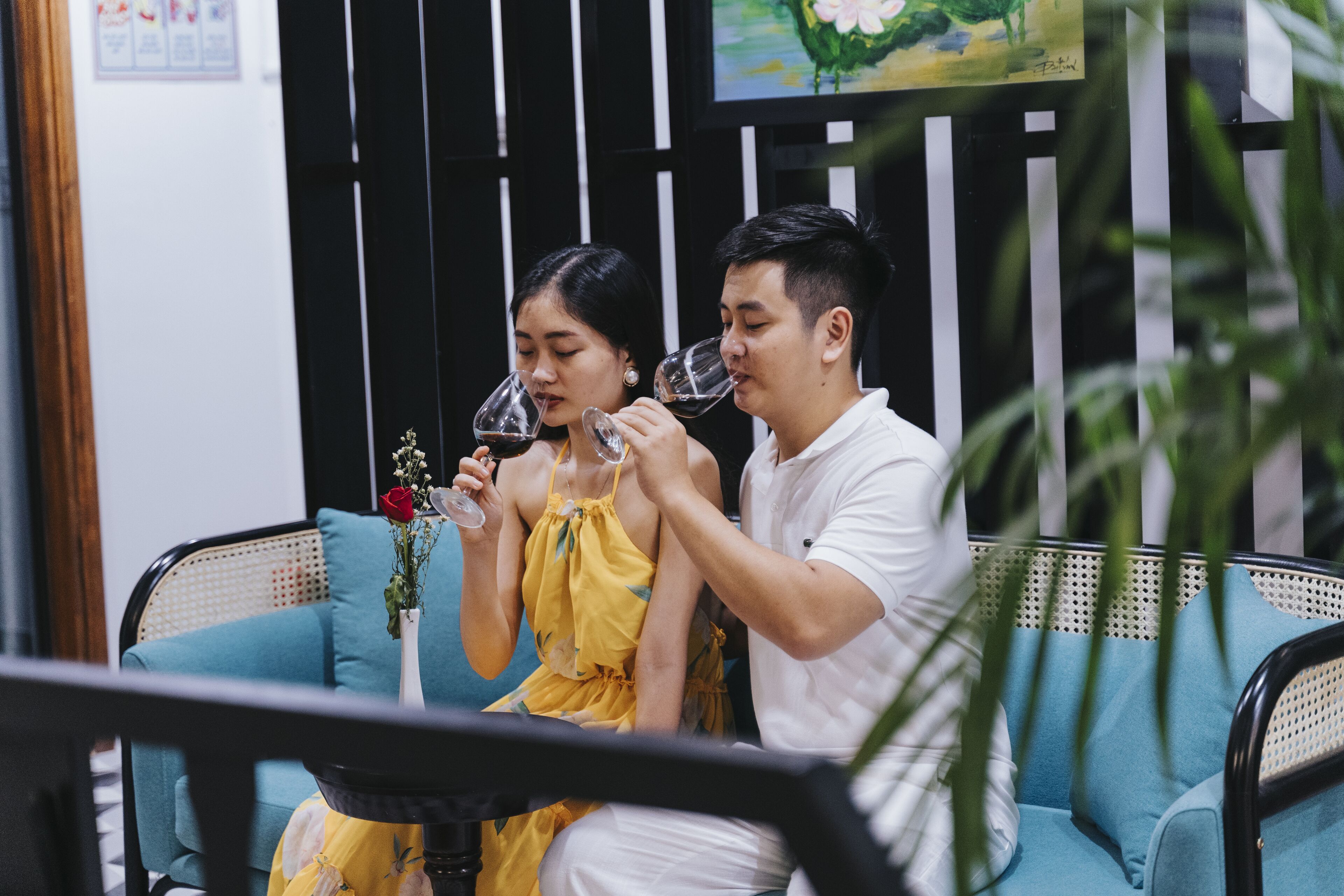 A couple sitting on a blue sofa with a vase of flowers between them.