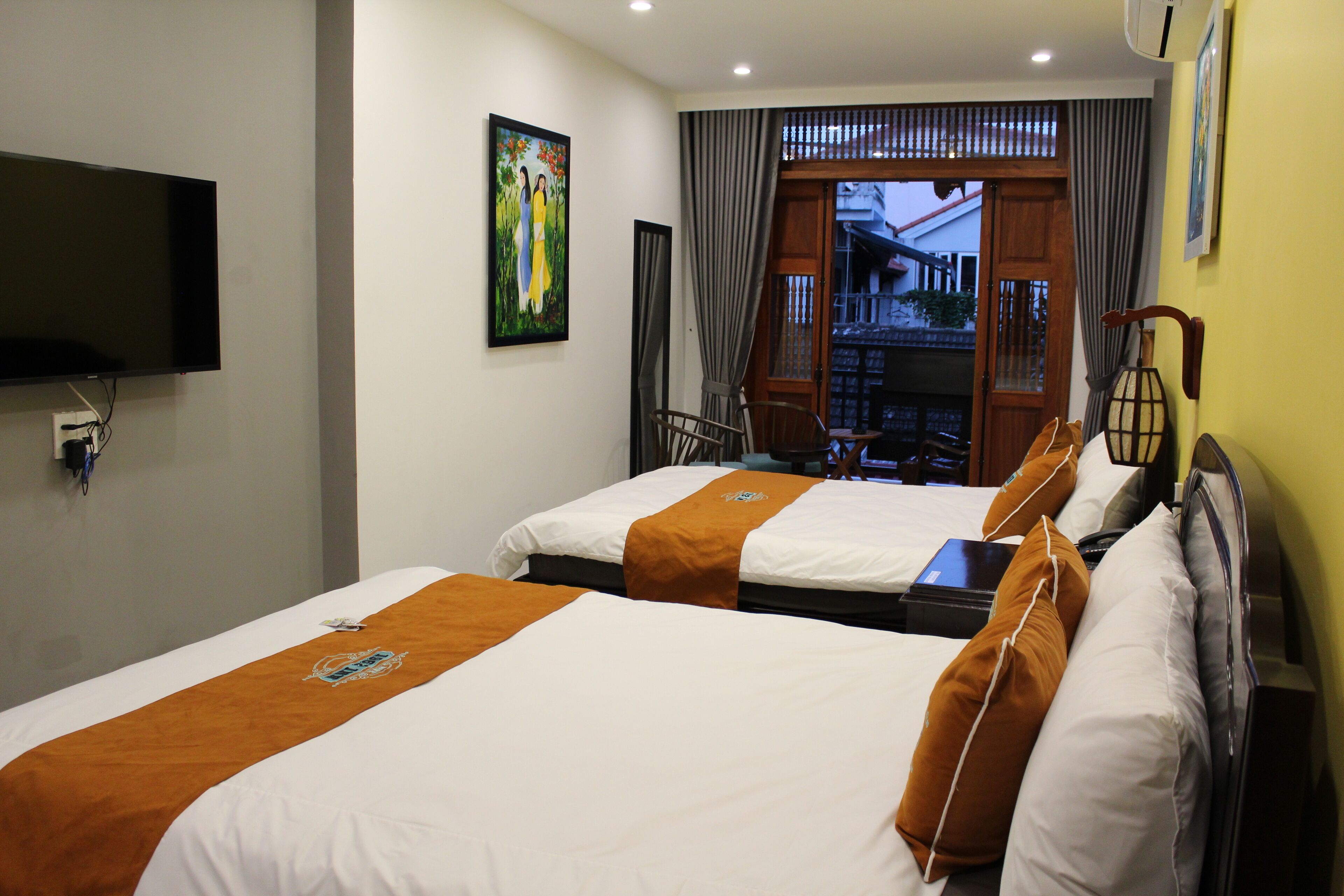 A hotel room with two beds, a flat-screen TV mounted on the wall, a painting, and a view of the outside through a door.