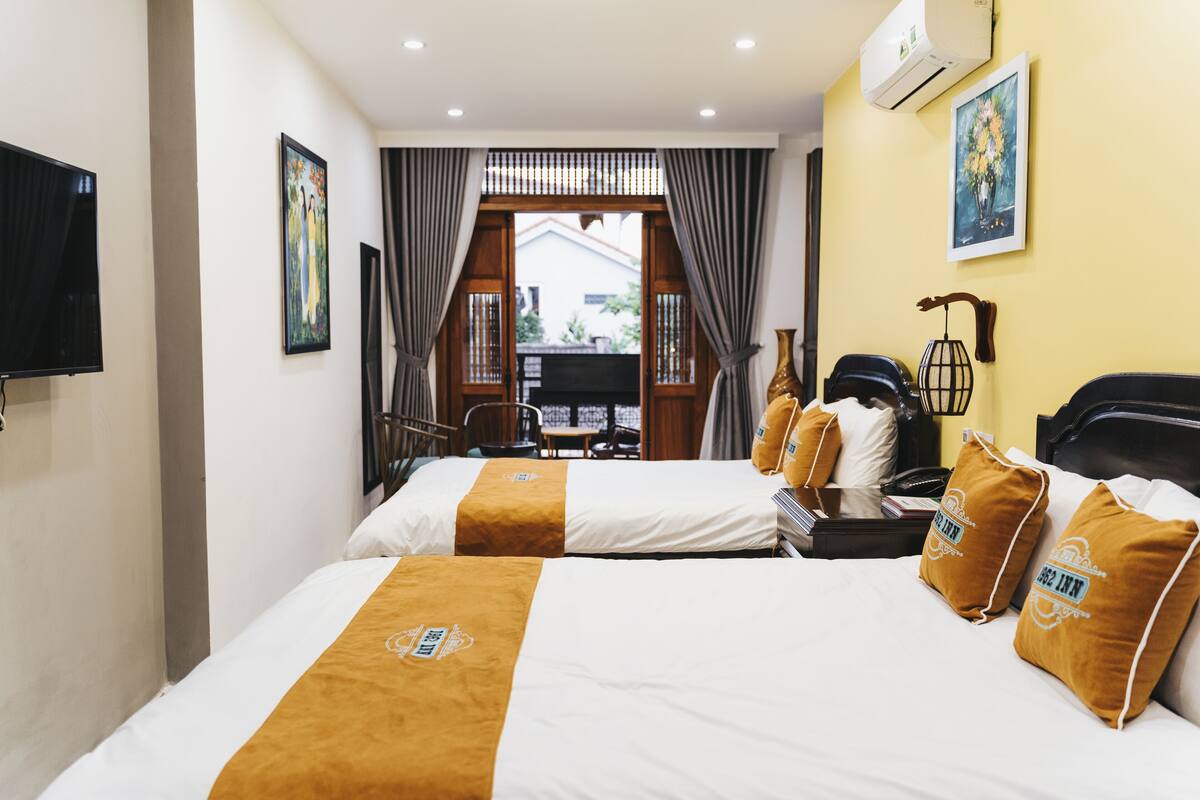 A hotel room with two beds, a TV, a desk, and a view of the outside.