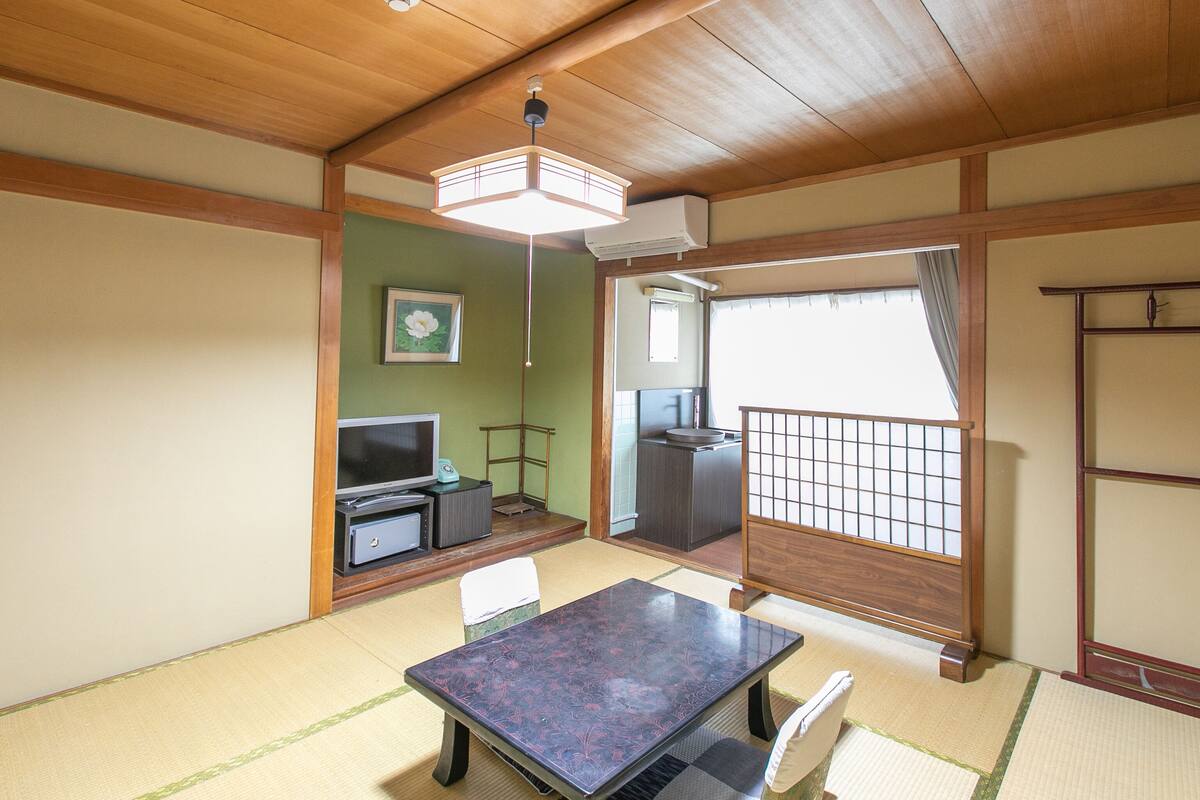 A traditional Japanese room with tatami flooring, a low table, a television, and a sliding door.