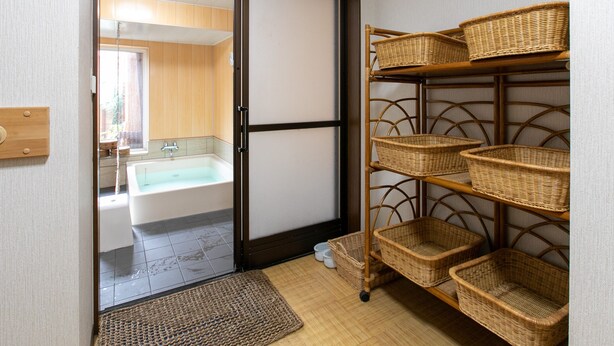A bathroom with a bathtub, a toilet, and a sink. There is a shelf with baskets and a woven mat at the entrance. - Tabist Matsuekan (Matsue)