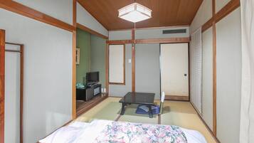 Une pièce de style japonais traditionnel, avec un sol recouvert de tatamis, un lit agrémenté d’une couvre-lit à motifs floraux, un téléviseur posé sur une petite table et des portes coulissantes.