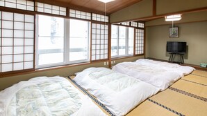 A traditional Japanese-style room with tatami flooring, a futon bed, sliding shoji doors, and a television on a stand. - Tabist Matsuekan (Matsue)