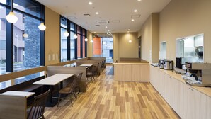 A modern cafe with wooden flooring, long communal tables, and hanging pendant lights.