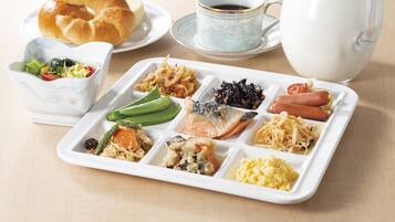Un plateau repas contenant divers aliments, un croissant, une tasse de café et une carafe de lait.