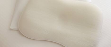 Un almohadón blanco y una funda de almohada blanca sobre una cama blanca.