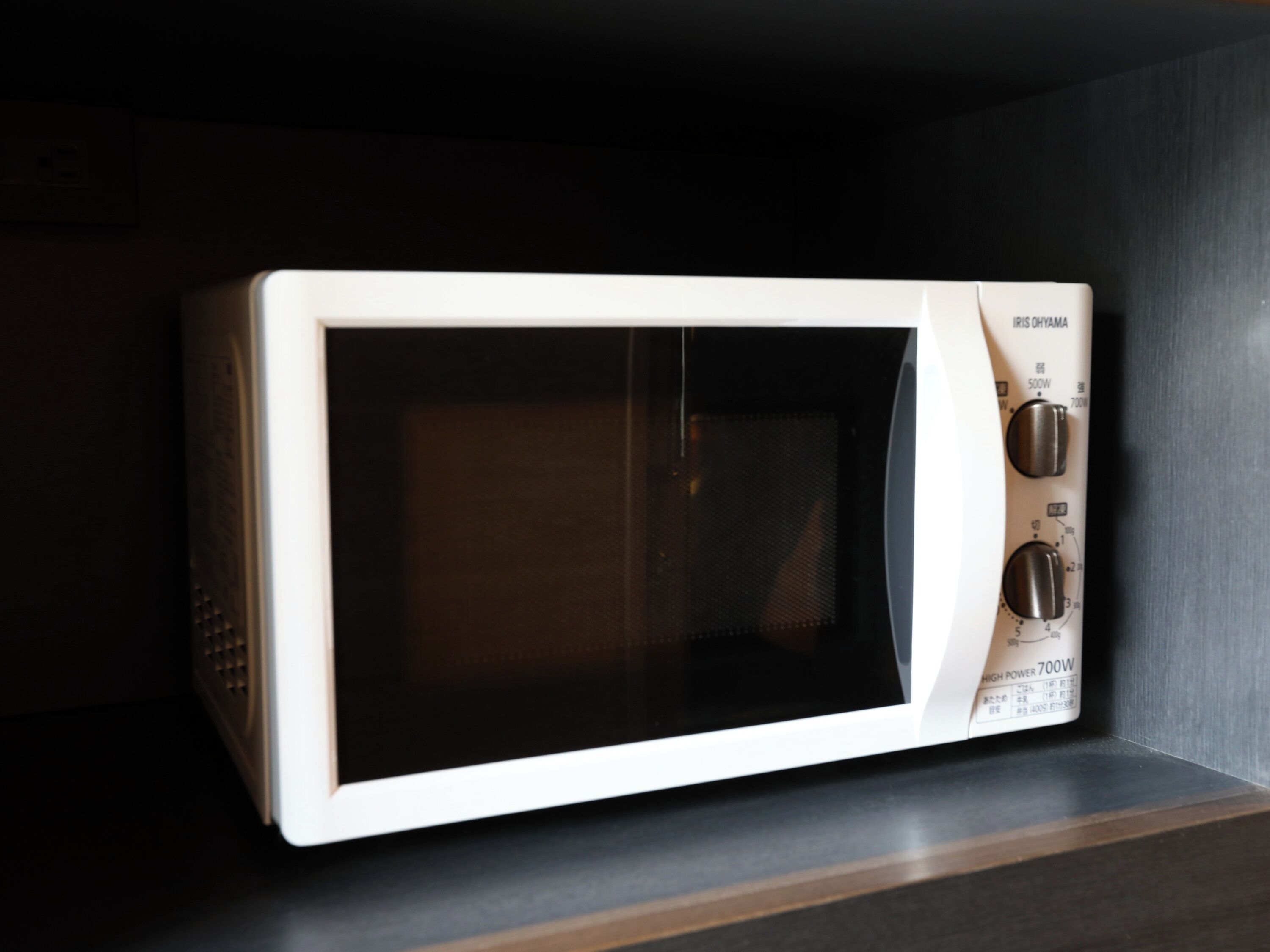 A white microwave oven with a digital display and control knobs, placed on a dark countertop.