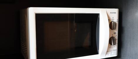 A white microwave oven with a digital display and control knobs, placed on a dark countertop.