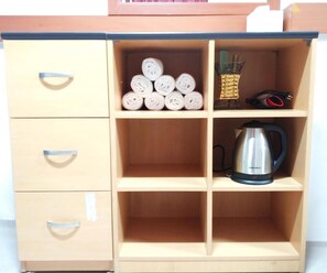Un mueble de madera con cuatro cajones y una repisa que contiene toallas enrolladas, una cesta pequeña y una tetera.