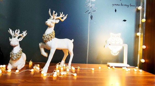 Two white deer figurines with antlers, one standing and one sitting, on a wooden surface with string lights. - Healinghouse Peakjang (Buyeo)