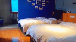 A room with two beds, a blue wall with pictures, wooden flooring, and a window with a flower design. - Happy Times Theme Inn (Deqin)