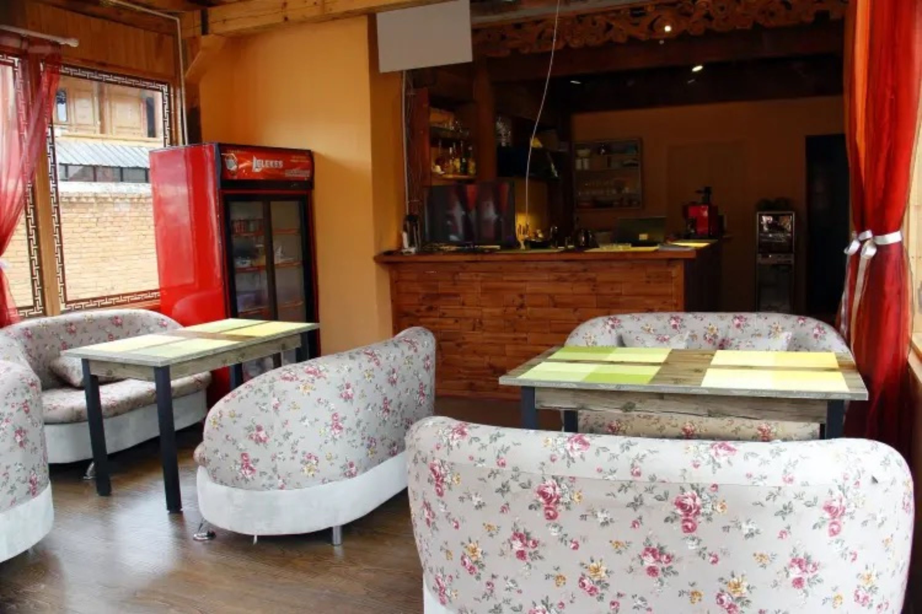 A cozy room with floral-patterned sofas and a wooden table, a red refrigerator, and a bar area with a counter.
