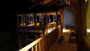 A wooden deck with a railing, a covered seating area with purple curtains, and a dog walking on the deck. - Happy Times Theme Inn (Deqin)