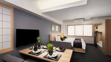 Una habitación de hotel moderna con televisor de pantalla plana, una cama con cabecero de madera, una zona de comedor con una mesa preparada para dos personas y una ventana con vistas a la ciudad.