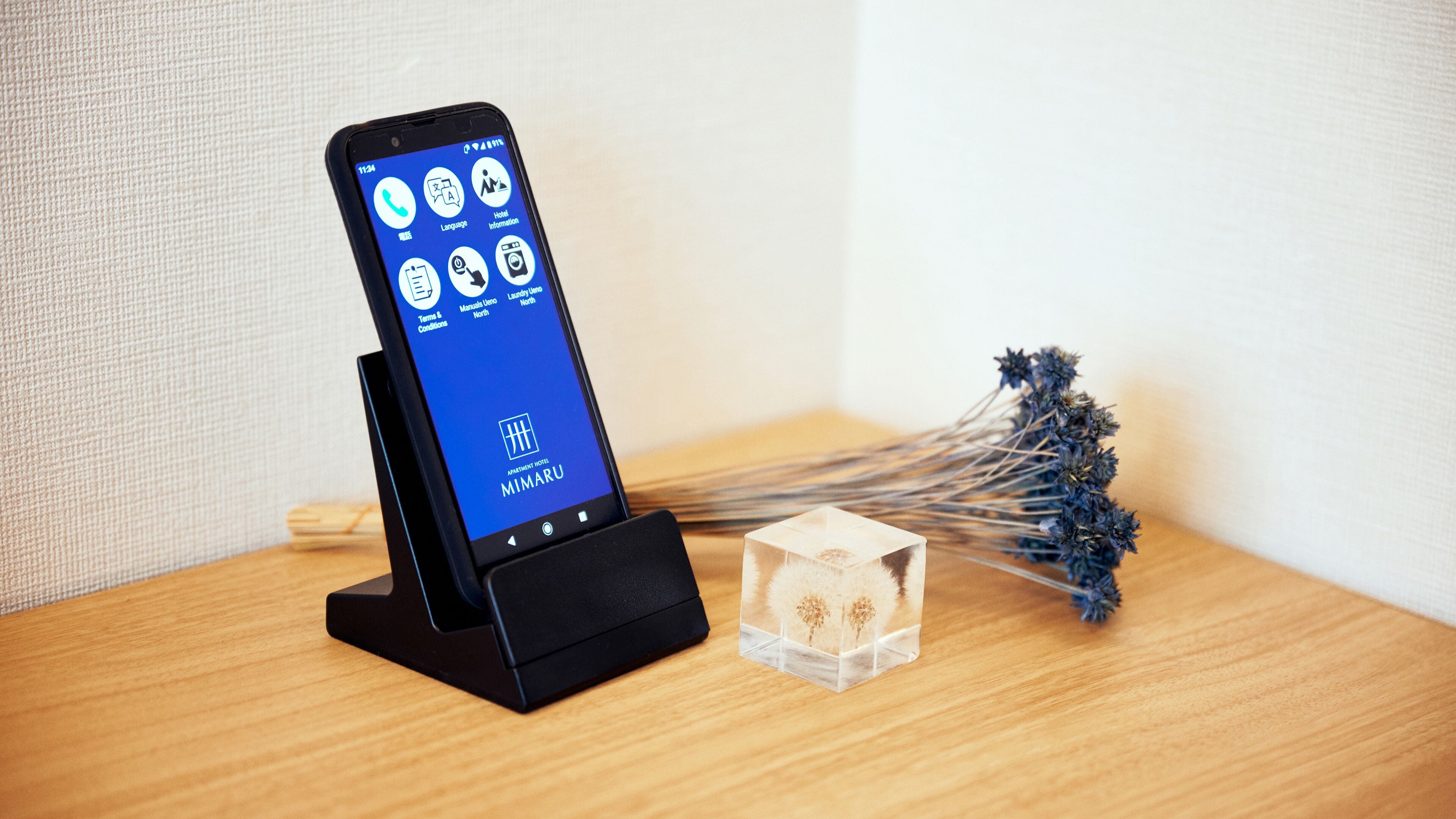Ein Smartphone auf einem Ständer, das eine Hotel-App mit Optionen wie 'Sprache', 'Hotelinformationen' und 'Waschservice' anzeigt.