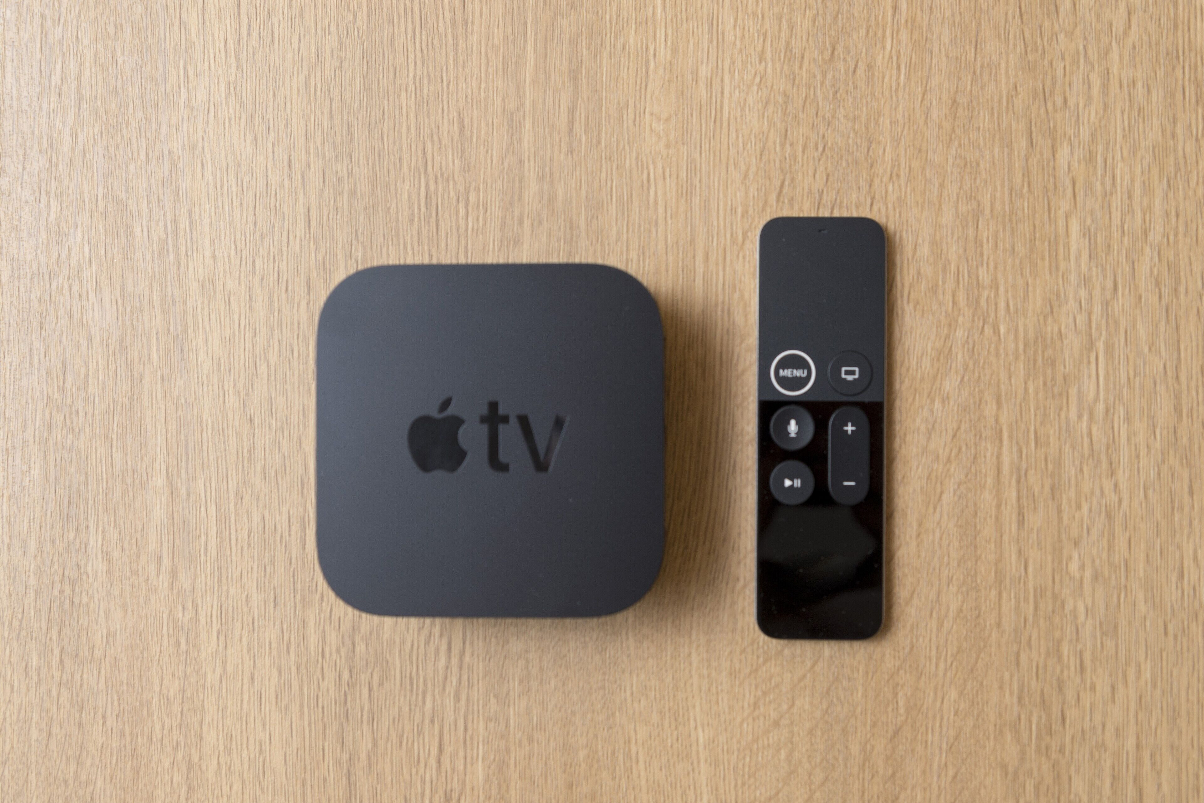 Um Apple TV e controle remoto sobre uma superfície de madeira.