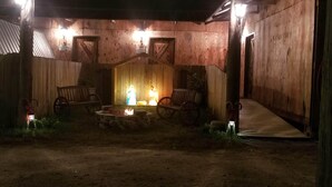 Un espacio al aire libre rústico con una chimenea, bancos de madera y un pequeño altar con velas.