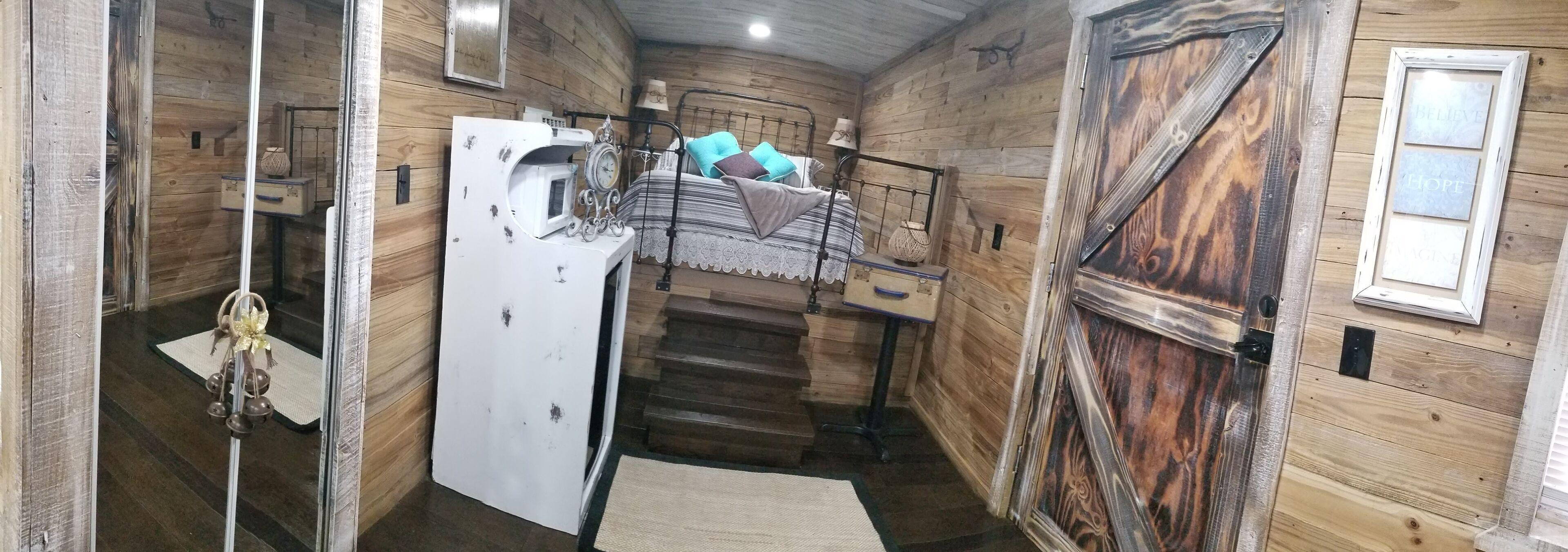 Un intérieur rustique en bois, avec un lit superposé, un réfrigérateur blanc et une grande porte en bois.