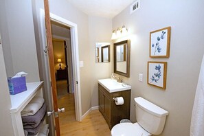 A compact bathroom with a toilet, sink, and two mirrors. A towel rack and a framed picture are visible.