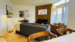 A cozy living room with a grey sofa, wooden dining table, and chairs. A fireplace is visible in the background, and there are framed pictures on the wall. - Newly Updated Cozy Condo in the Heart of Wintergreen!  Pet friendly. (Wintergreen)