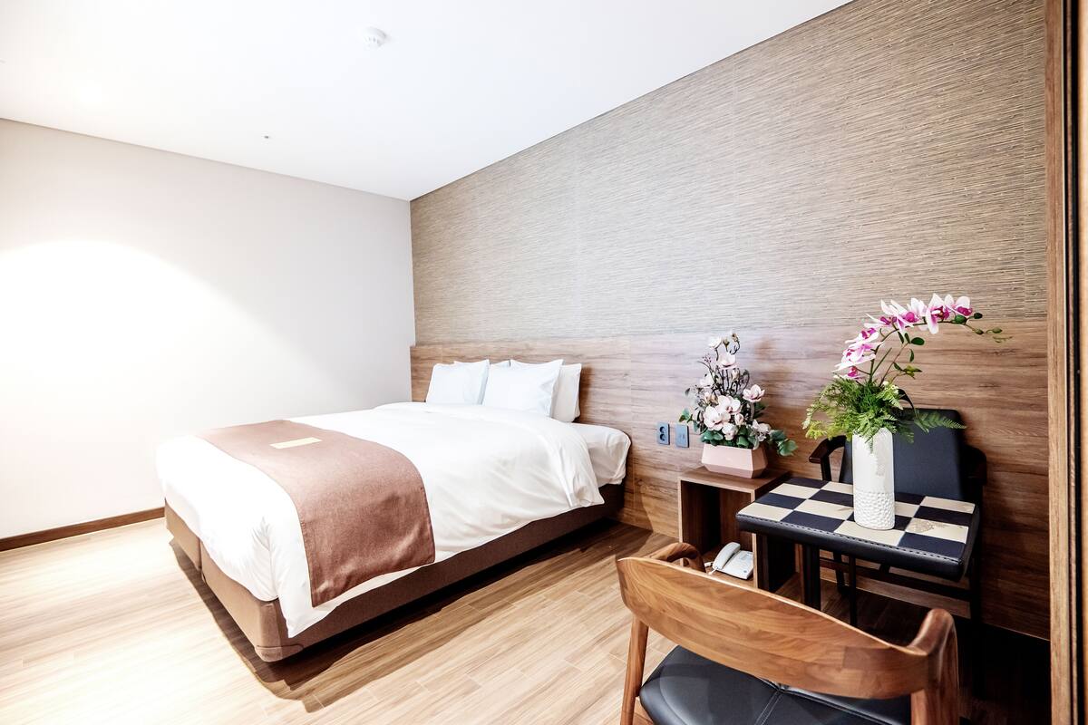 A modern hotel room with a wooden bed, a small table with a vase of flowers, and a chair.