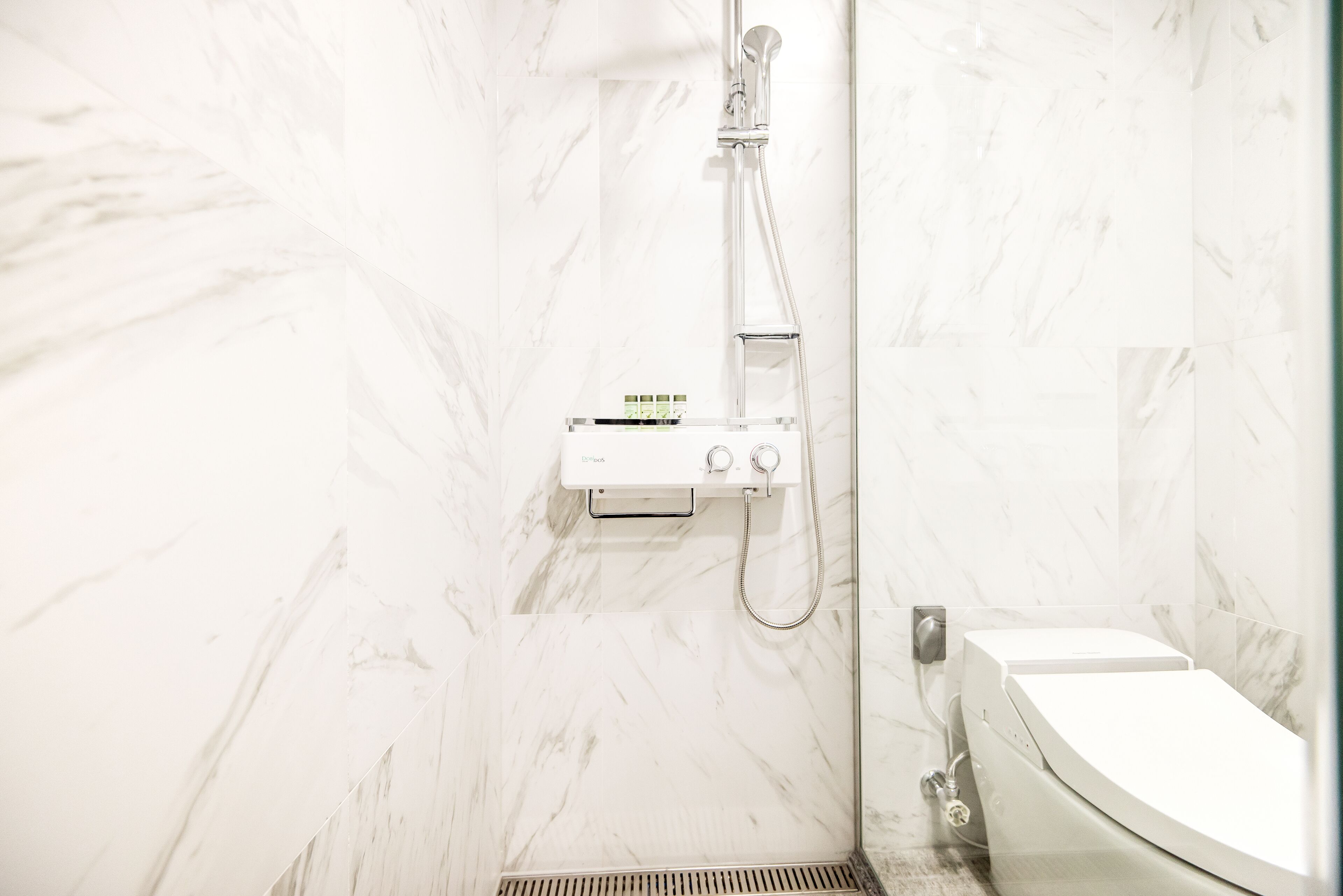Un baño con inodoro blanco, ducha con cabezal de ducha manual y panel de control.