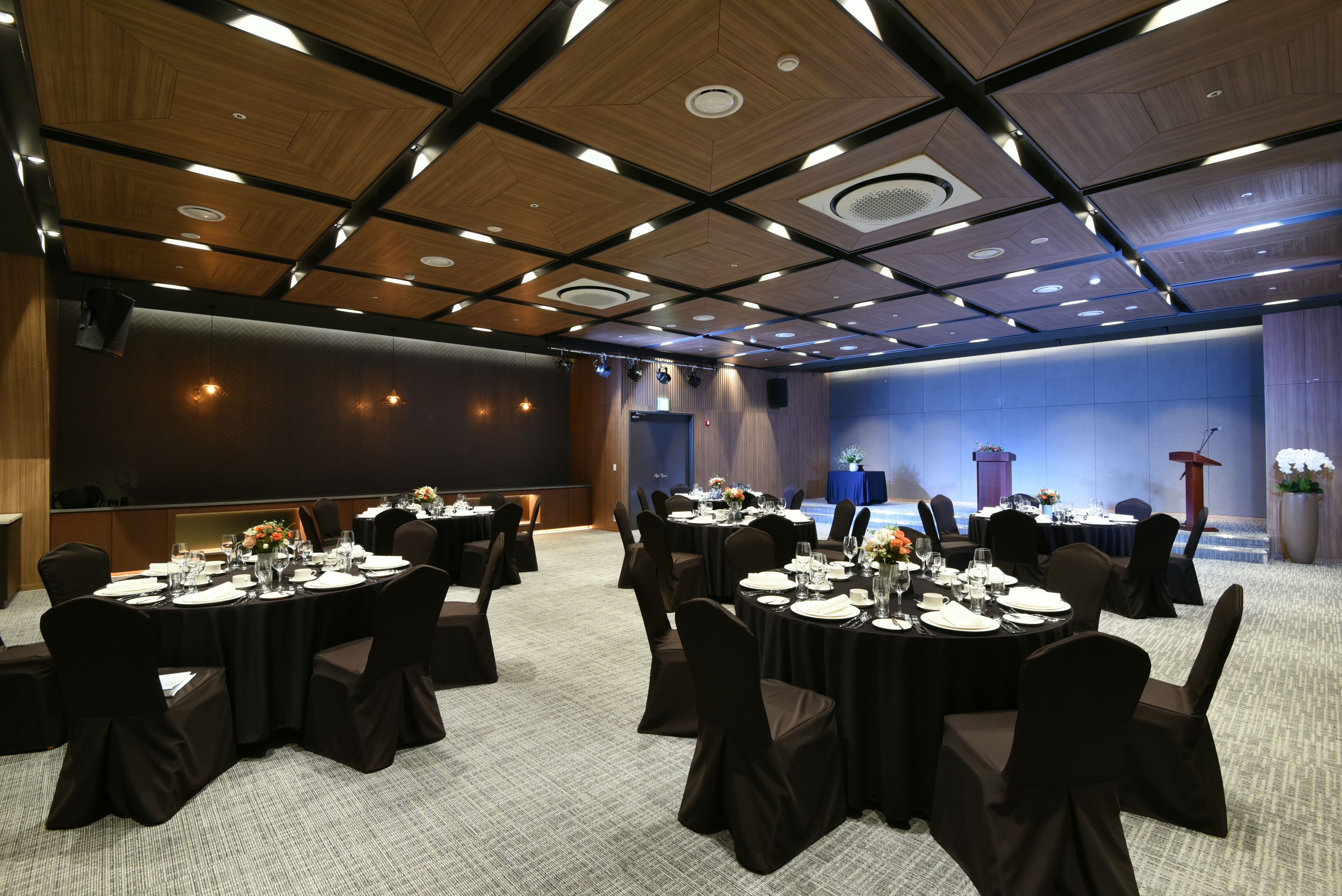 A conference room with round tables, black chairs, and a stage with a podium.