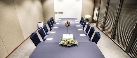 Un salón de conferencias con una larga mesa, sillas, un proyector y una decoración floral.