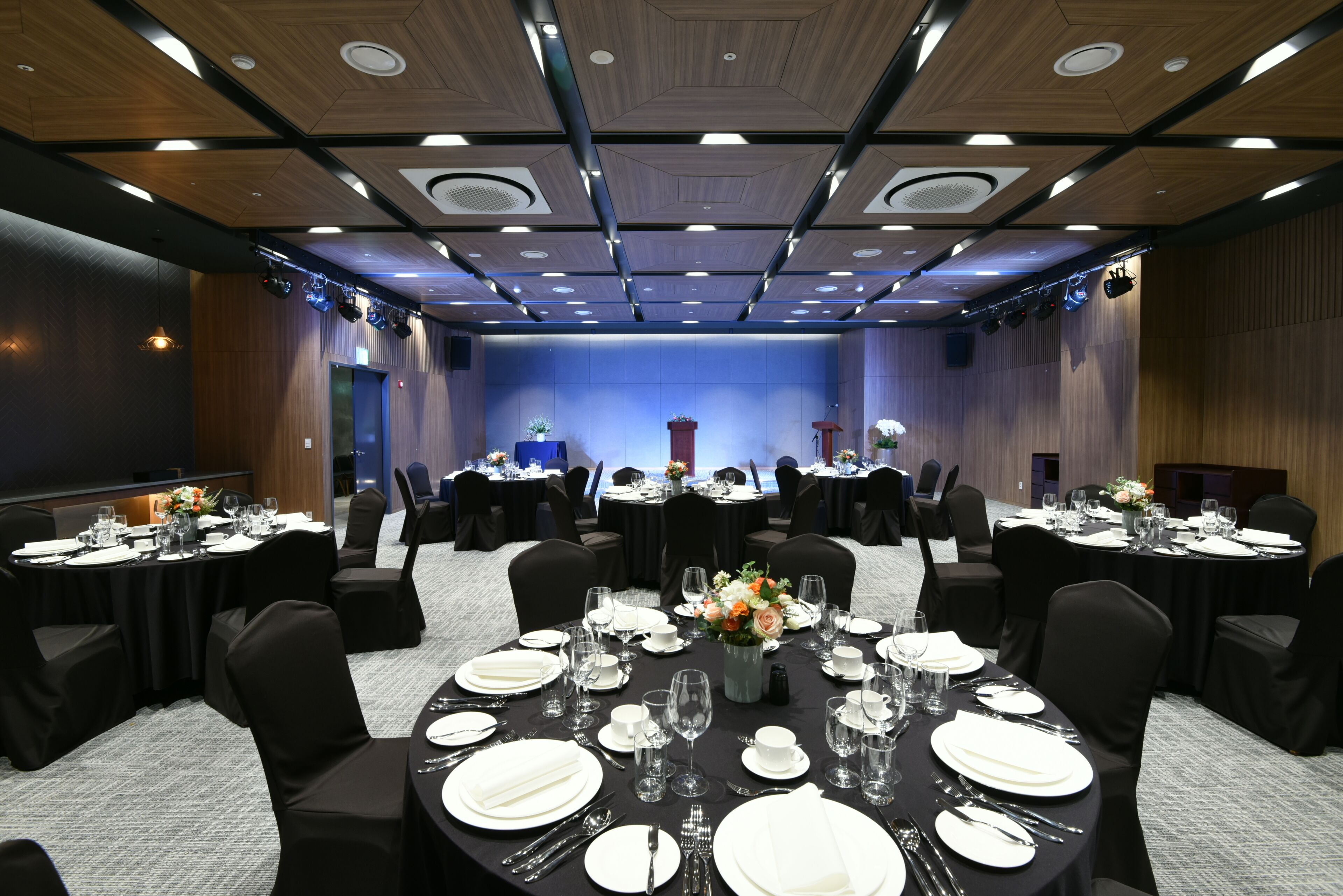 A conference room with round tables, black chairs, and a stage with a podium.
