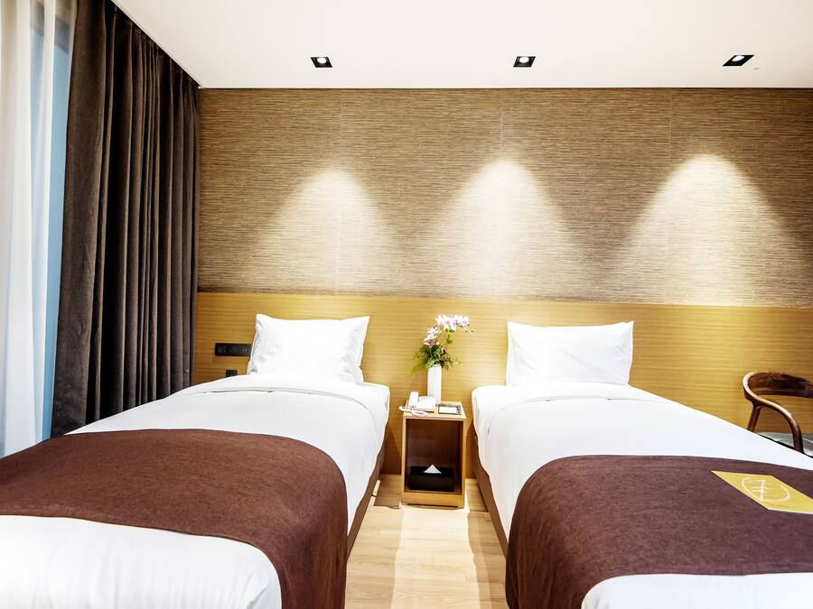A hotel room with two beds, a wooden headboard, a nightstand with a phone and a vase of flowers, and a chair.