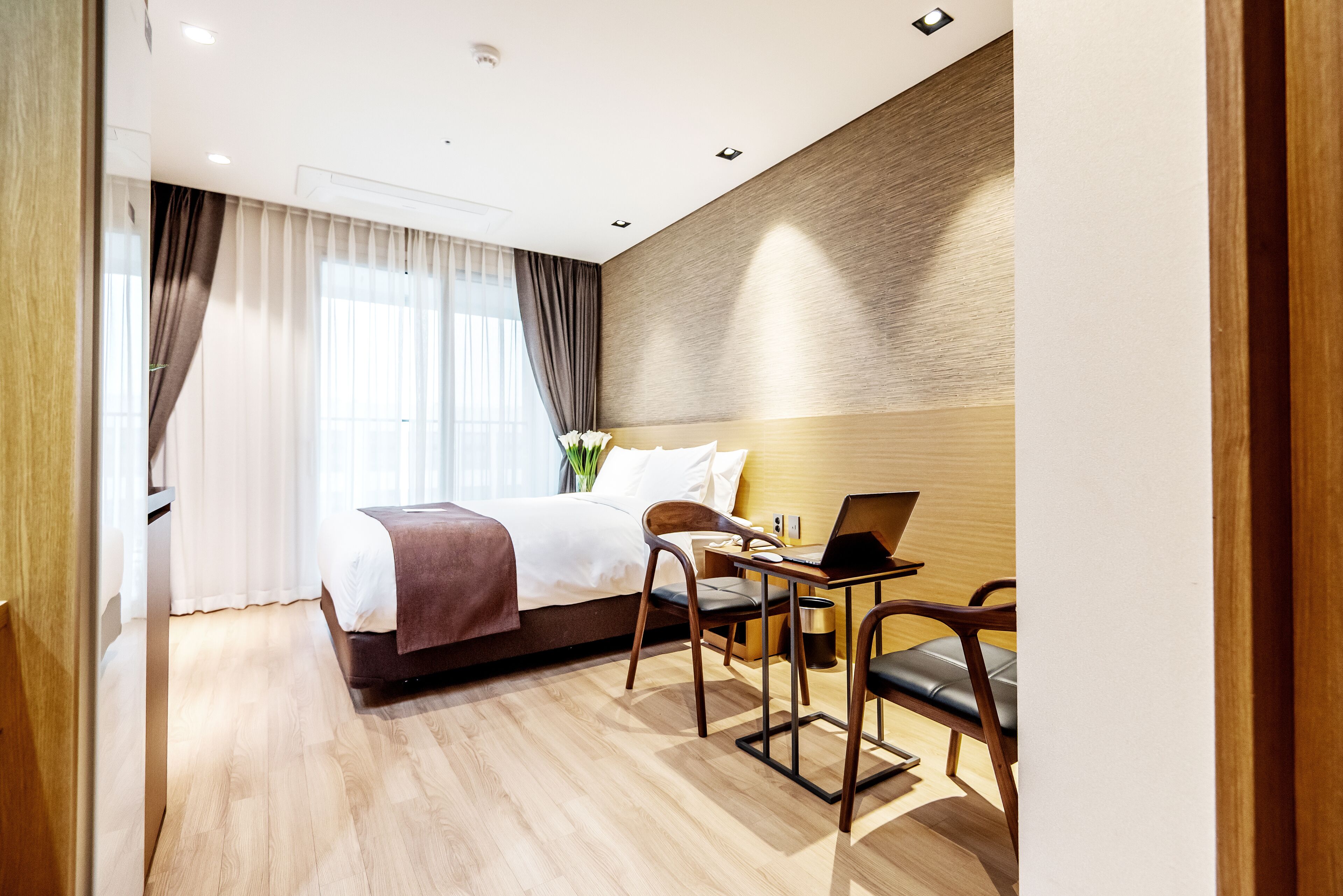 A hotel room with a bed, a desk with a laptop, and a chair.