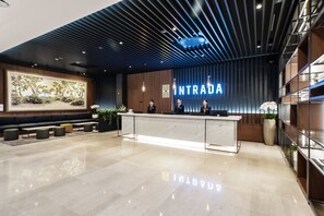Una recepción moderna con un mostrador de mármol, una obra de arte grande enmarcadas y un letrero que dice “INTRADA”.