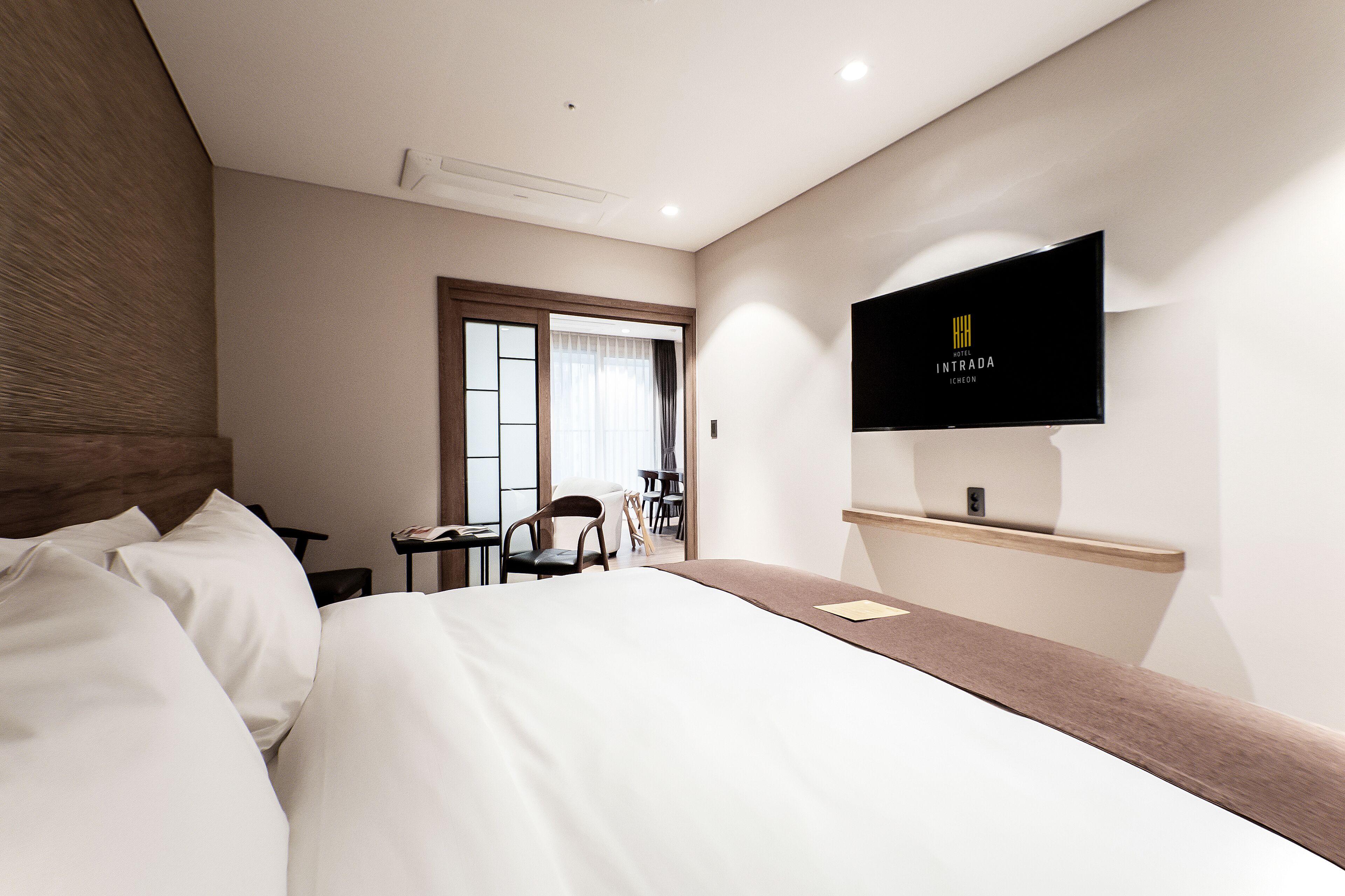 Et hotelværelse med en seng, et tv ophængt på væggen, et skrivebord og en stol.