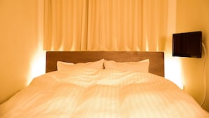 Una cama bien hecha con sábanas blancas, cabecera de madera y un televisor montado en la pared.