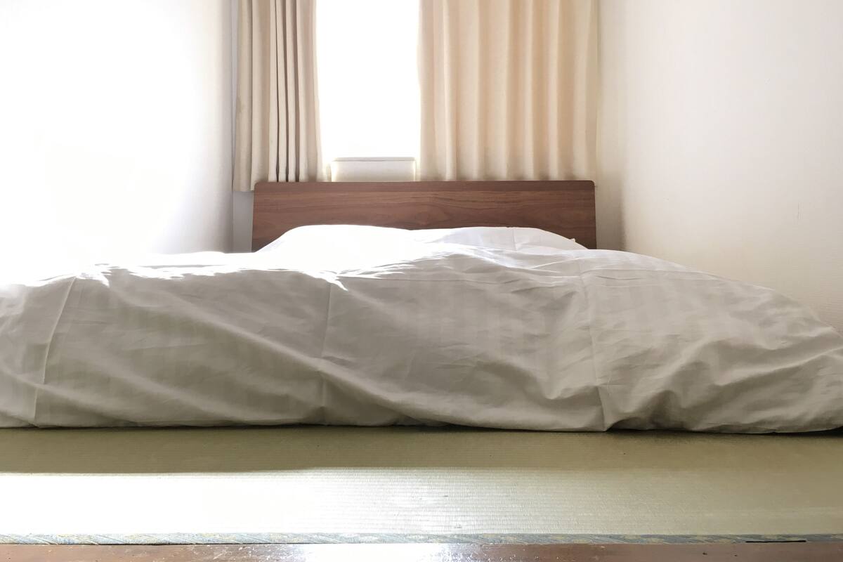 A bed with a wooden headboard, white bedding, and a window with curtains.