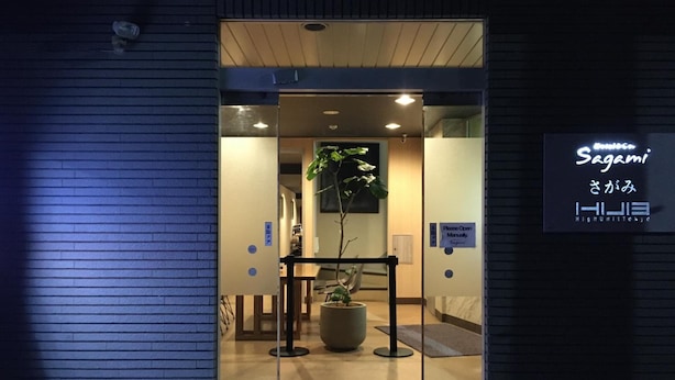 Entrada de un hotel con puerta de cristal, una planta en maceta en el interior y un cartel con el nombre del hotel.