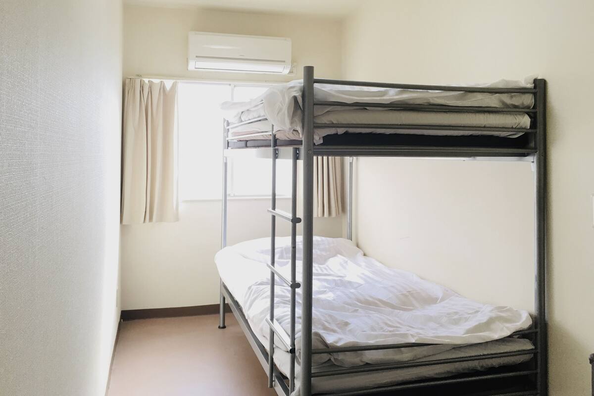 A bunk bed room with a window, curtains, and an air conditioning unit.