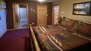 A bedroom with a large bed, a ceiling fan, a door leading to another room, and a painting on the wall. - Peaceful Meadows (Custer)