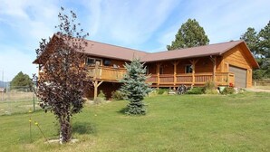 A two-story wooden cabin with a balcony, a garage, and a well-maintained lawn. - Peaceful Meadows (Custer)