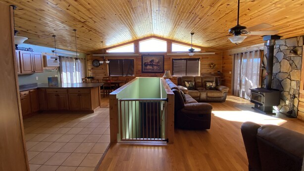 A spacious cabin interior with a wooden ceiling, a central island, a stone fireplace, and a dining area. - Peaceful Meadows (Custer)