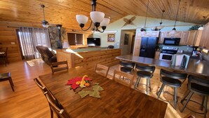 A spacious kitchen with wooden cabinetry, a central island with bar stools, and a dining area with a wooden table and chairs. - Peaceful Meadows (Custer)