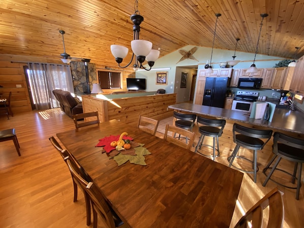 A spacious kitchen with wooden cabinetry, a central island with bar stools, and a dining area with a wooden table and chairs. - Peaceful Meadows (Custer)