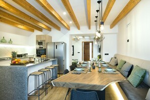 A modern kitchen with wooden beams, a central island with stools, and a dining area with a long table set for six.
