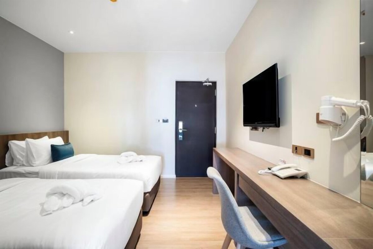 Habitación de hotel con dos camas, un escritorio con teléfono y secador de pelo, televisión y puerta.